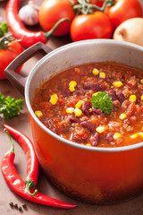 mexican chili con carne in red rustic pot with ingredients