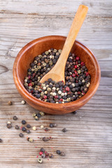 Peppercorns in bowl with a wooden spoon on a rustic table