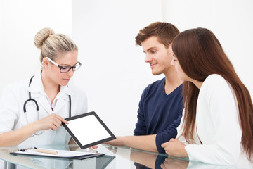 Doctor Showing Report To Couple On Digital Tablet