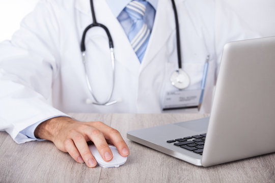 Midsection Of Doctor Using Laptop And Mouse At Desk