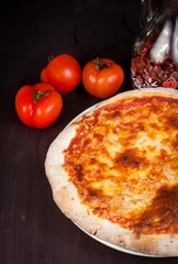 Delicious fresh pizza near tomatoes and spicy oil
