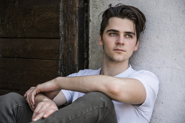 Attractive young man sitting on old door's threshold