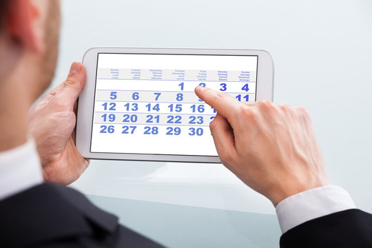 Businessman Touching Calendar Date On Digital Tablet In Office