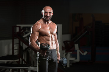 Fototapeta na wymiar Mature Bodybuilder Exercising Biceps With Dumbbell