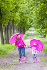 mother and her daughter with umbrellas in spring alley
