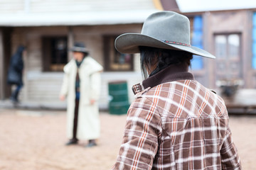 Cowboy with hat standing against another man in street