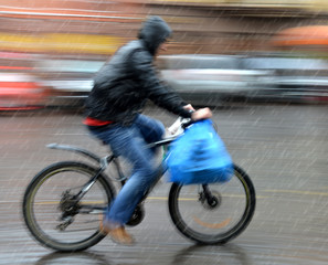 Fototapeta premium Cyclist in motion riding down the street on rainy day