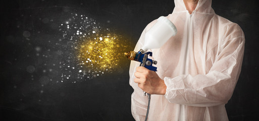 Worker with airbrush painting with glowing golden paint
