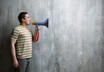 Emotional man shouts through a megaphone on a background of gray