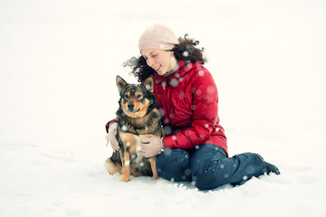 Happy young woman sitting and hugging dog in snowstorm