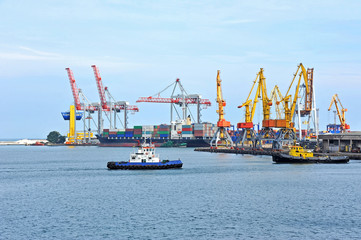 Tugboat assisting container cargo ship to harbor quayside