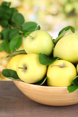 Ripe sweet apples with leaves in wooden bowl