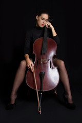 Beautiful brunette holding cello with selective light in black d
