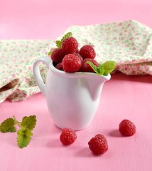 Ripe raspberries in a white jug on pink background