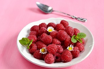 Ripe raspberries in a white plate with a spoon