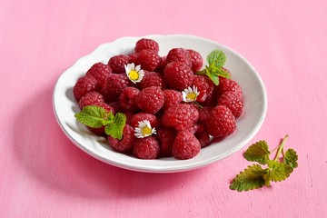Ripe raspberries in a white plate with mint