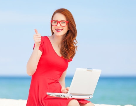 Redhead girl in the glasses with notebook on the beach