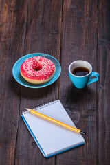Cup of coffee with notebook and donut.