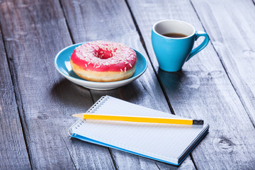 Cup of coffee with notebook and donut.