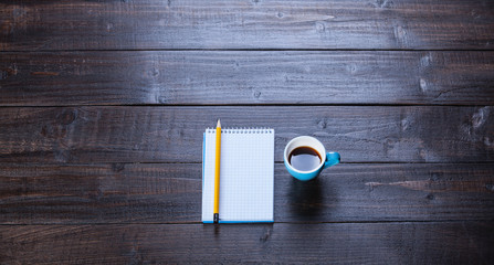 Cup of coffee with notebook and pencil, on wooden table.