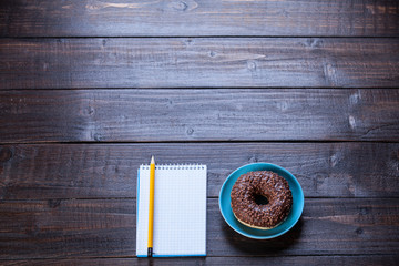 Notebook, donut and pencil on wooden table.