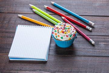 Naklejka premium Pencils, cupcake and notebook on wooden table