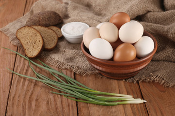 Obraz na płótnie Canvas raw eggs in an earthenware bowl, onions, bread, salt shaker