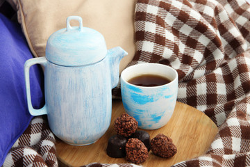 Cup and teapot with candies on wooden stand on bed close up