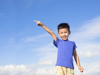 happy little boy pointing direction with blue sky background