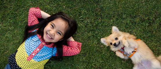 Happy Asian girl with her doggy portrait lying on lawn © RedcupStudio