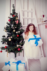 Happy smiling kid holding gifts near the Christmas tree.