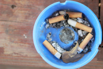 cigarette butts in an ashtray on a wood floor.