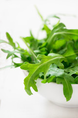 Fresh arugula in bowl over light  background