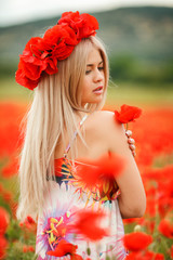 Beautiful young blonde woman in red bright poppy field.