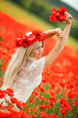Beautiful young blonde woman in red bright poppy field.