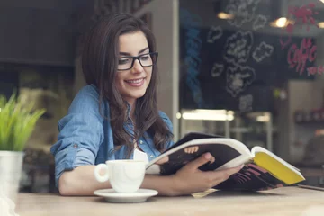 Crédence de cuisine en verre imprimé Restaurant Smiling woman reading newspaper at cafe