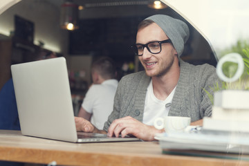 Handsome hipster using laptop at cafe
