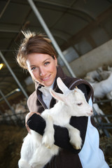 Cheerful farmer woman carrying baby goat in barn