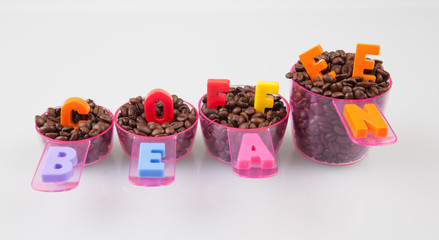 Fototapeta na wymiar Coffee beans in measuring cups of various sizes on white