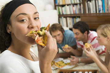 Vier junge Leute liegen auf dem Boden,essen Pizza