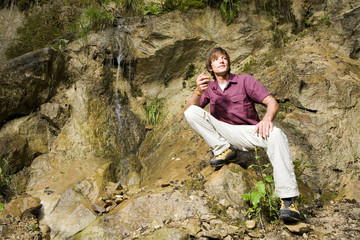 Naklejka na ściany i meble Junger Mann sitzt mit Wasserfall,entfernt,suchen lächelnd
