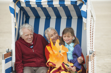 Deutschland,St. Peter-Ording,Nordsee,Mädchen (6-7 ) sitzen bei den Großeltern auf Strandkorb