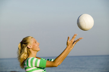 Junge Frau spielt mit Ball am Strand,Seitenansicht