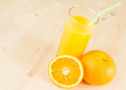 full glass of orange juice with straw near fruit orange