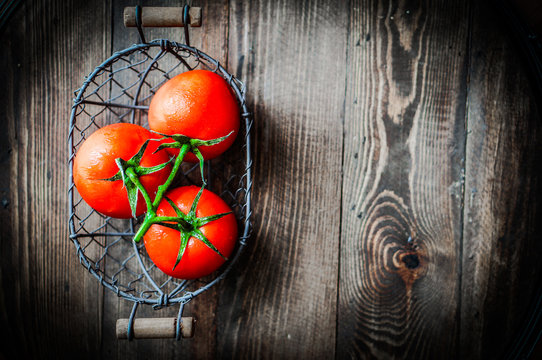 Fresh tomatoes in antique basket on wooden background