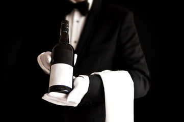 Waiter in tuxedo holding a bottle of red wine - obrazy, fototapety, plakaty