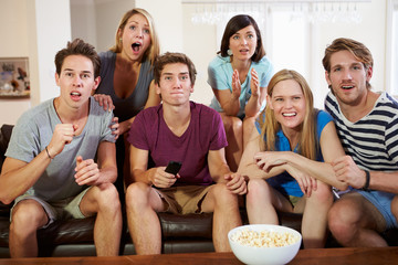 Obraz premium Group Of Friends Sitting On Sofa Watching TV Together