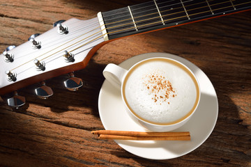 A cup of cappuccino and guitar on wooden table
