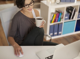 Smiling woman with cup of coffee using laptop at home