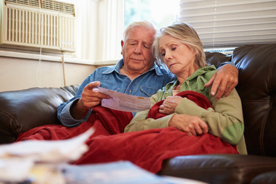 Worried Senior Couple Sitting On Sofa Looking At Bills